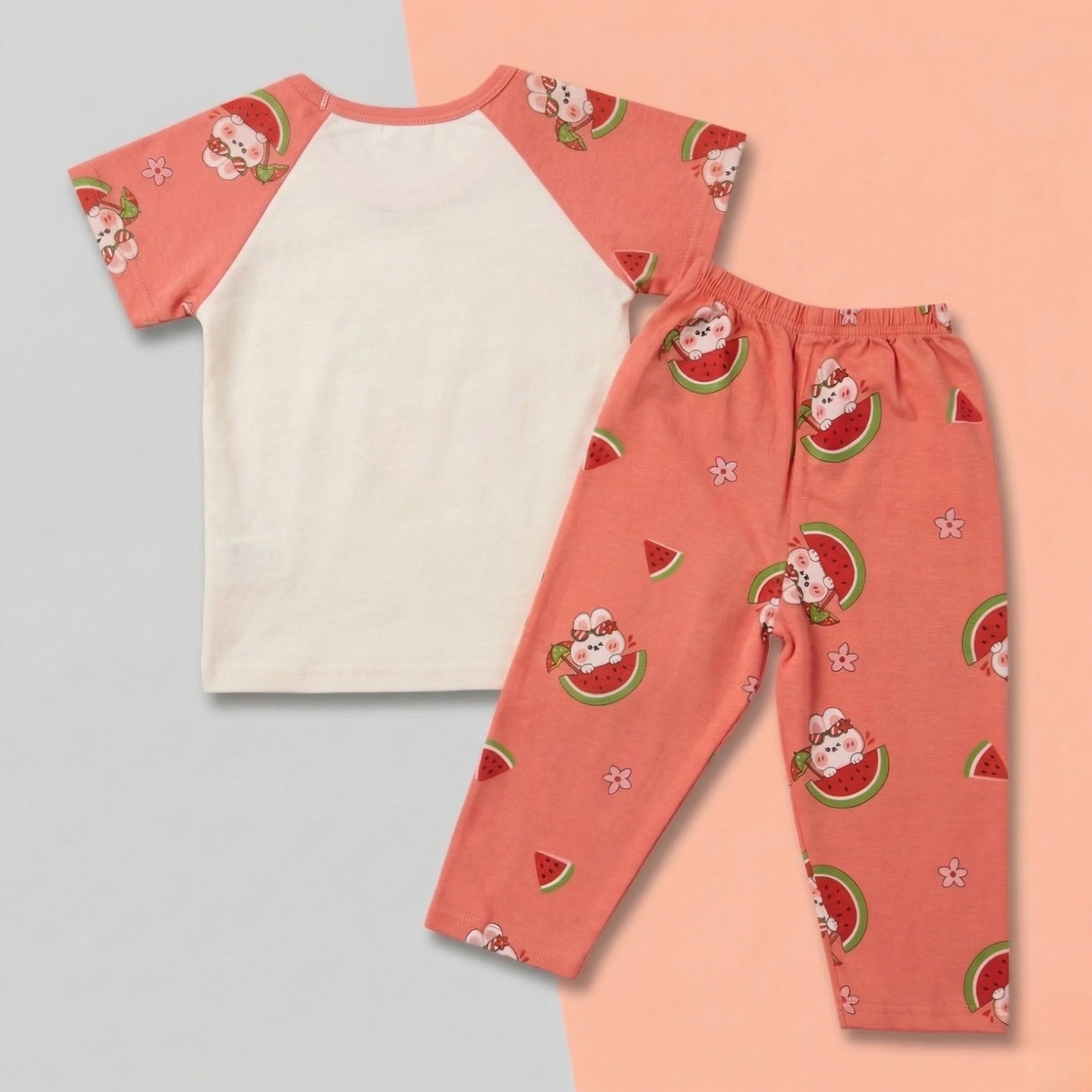 Children's pajama set with a pink and white top and pink pants featuring cartoon characters and watermelon slices on a two-tone background.
