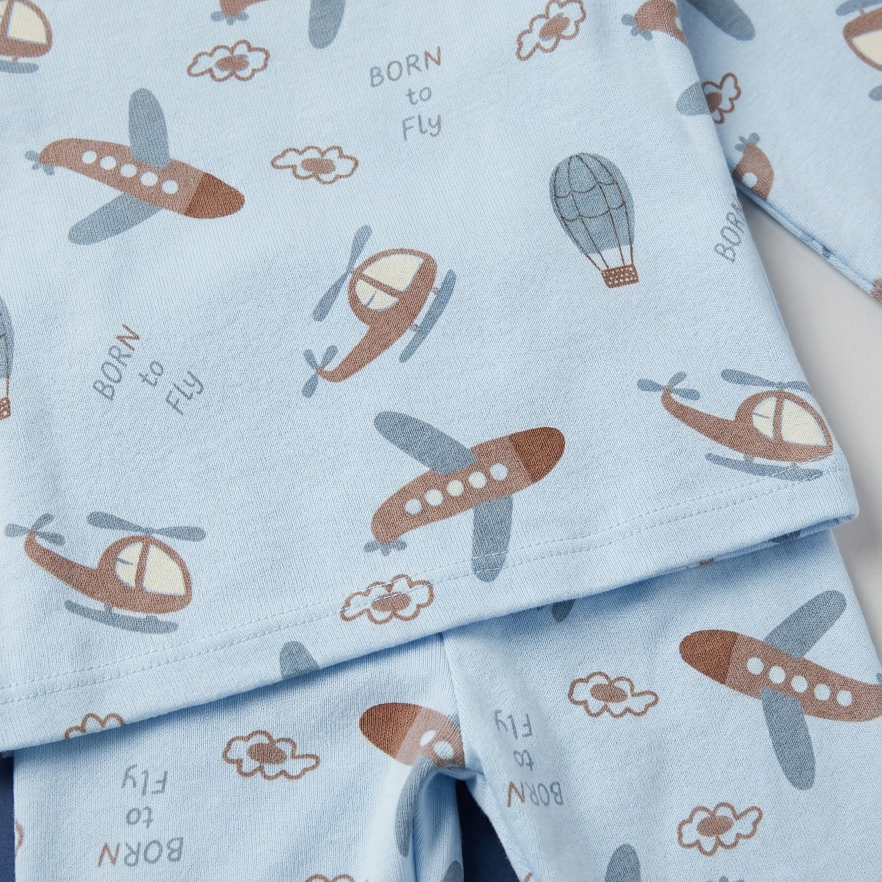 Children's pajama set with airplane and helicopter pattern on light blue fabric.